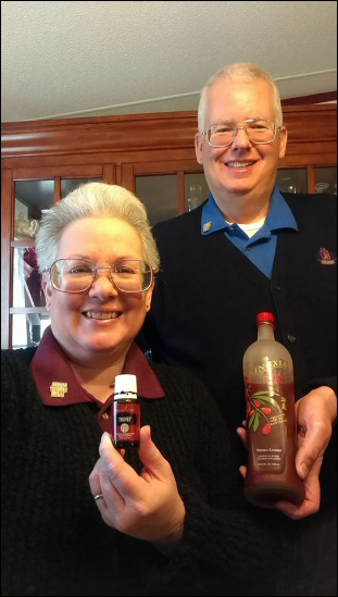 Mike and Vicki Simons holding Young Living products. Mike is holding a bottle of NingXia Red and Vicki is holding a bottle of Thieves essential oil blend.