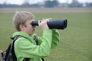 A boy looking through long binoculars, symbolizing someone looking for more, perhaps a better or bigger purpose.